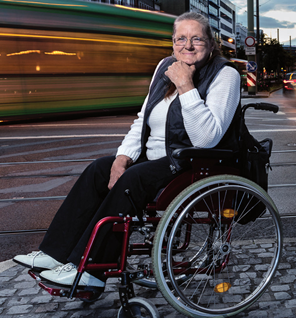 Petra Rieth sitzt in ihrem Rollstuhl an einer Straße und lächelt in die Kamera., © Stefan Freund für den traffiQ-Geschäftsbericht 2015